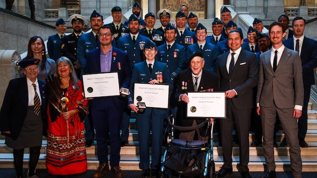 A group of people, both men and women, stand in a staircase, some of them holding a plaque.
