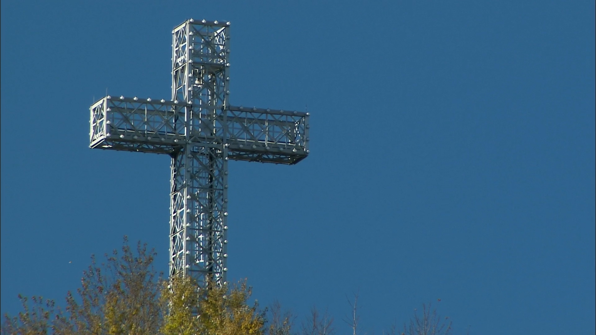 The cross on Montreal's Mount Royal may be turning 100, but its story begins in 1643; Montreal's metallic cross on Mt\. Royal with a blue sky behind and trees below