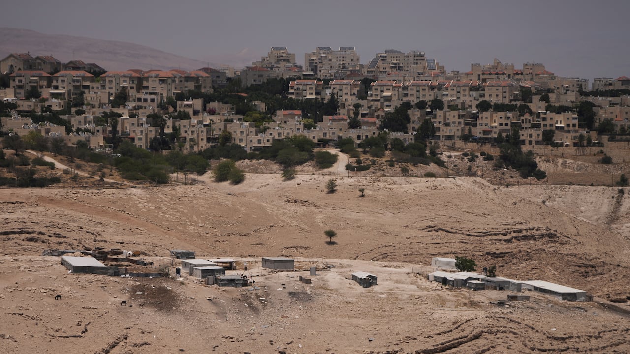 Steep hills in the foreground, dotted with several small, simple structures; In the middle distance, dozens of mid-rise apartment buildings.