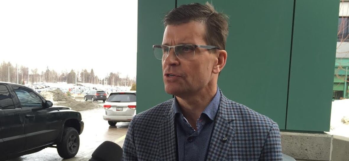 A antheral   with glasses speaks into a microphone successful  a infirmary  parking lot