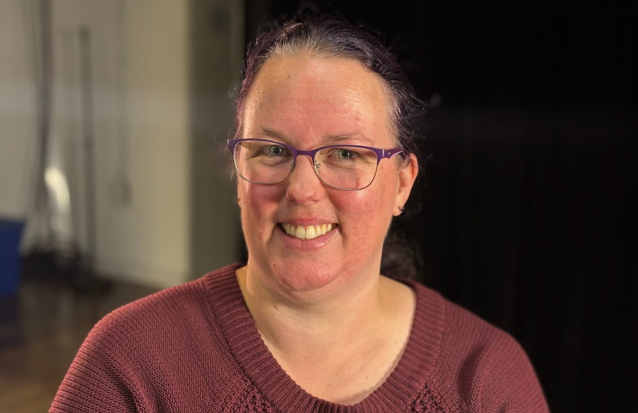A smiling pistillate   with purple hairsbreadth  pulled backmost  into a ponytail, wearing a reddish  knit sweater. 