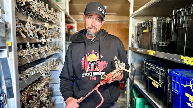 Dave Rockwood is Nova Scotia's fire and ground search and rescue co-ordinator, a new position with the Department of Emergency Management. A man in a baseball cap and hoodie stands amongst sprinkler heads on the wall and boxes and hold a sprinkler in his hand.