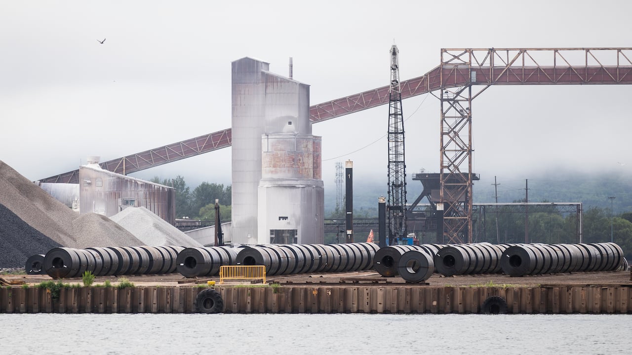 Rolled oils of steel sit in a yard at a steel company by a river on a foggy day.