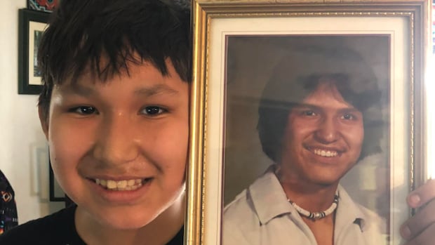 A young boy smiles as he holds up a framed photo of another man next to his face.