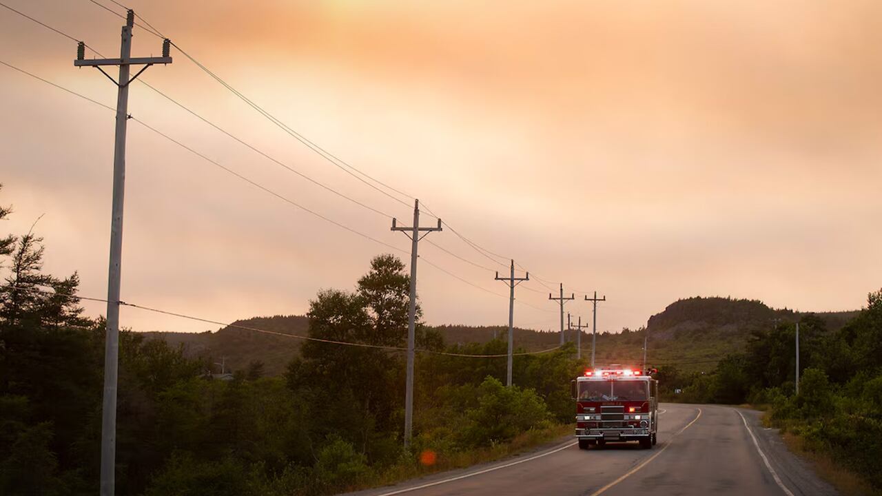 A fire truck on an empty road with a fiery sky behind it. 