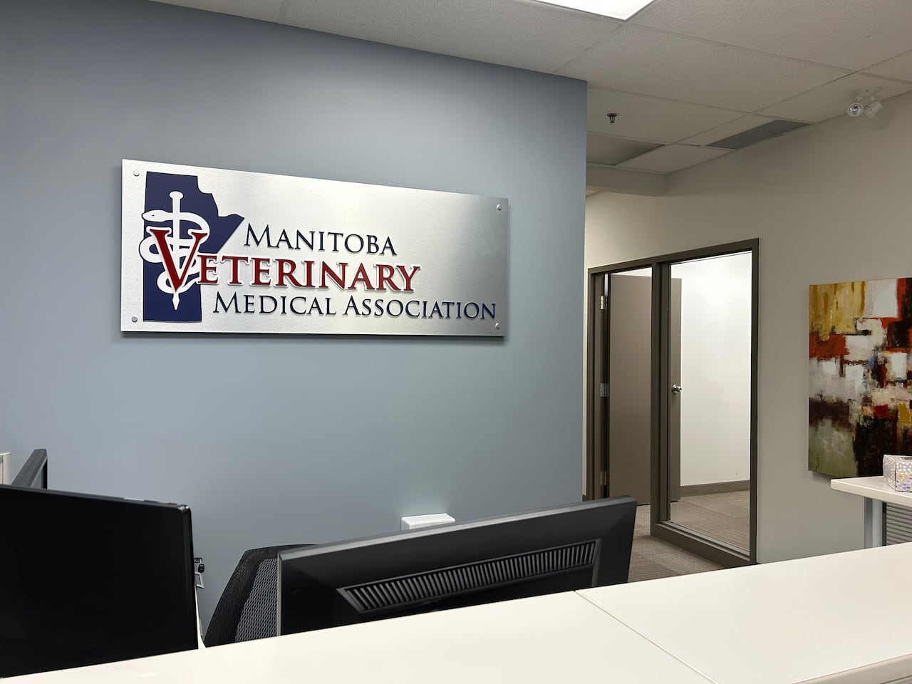 A sign on the wall inside an office says Manitoba Veterinary Medical Association with a graphic in the shape of Manitoba.