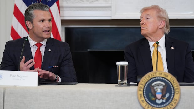 Defense Secretary Pete Hegseth speaks during a roundtable on criminal cartels with President Donald Trump in the State Dining Room of the White House, Thursday, Oct. 23, 2025, in Washington.  Two men sit at a table with a US flag behind