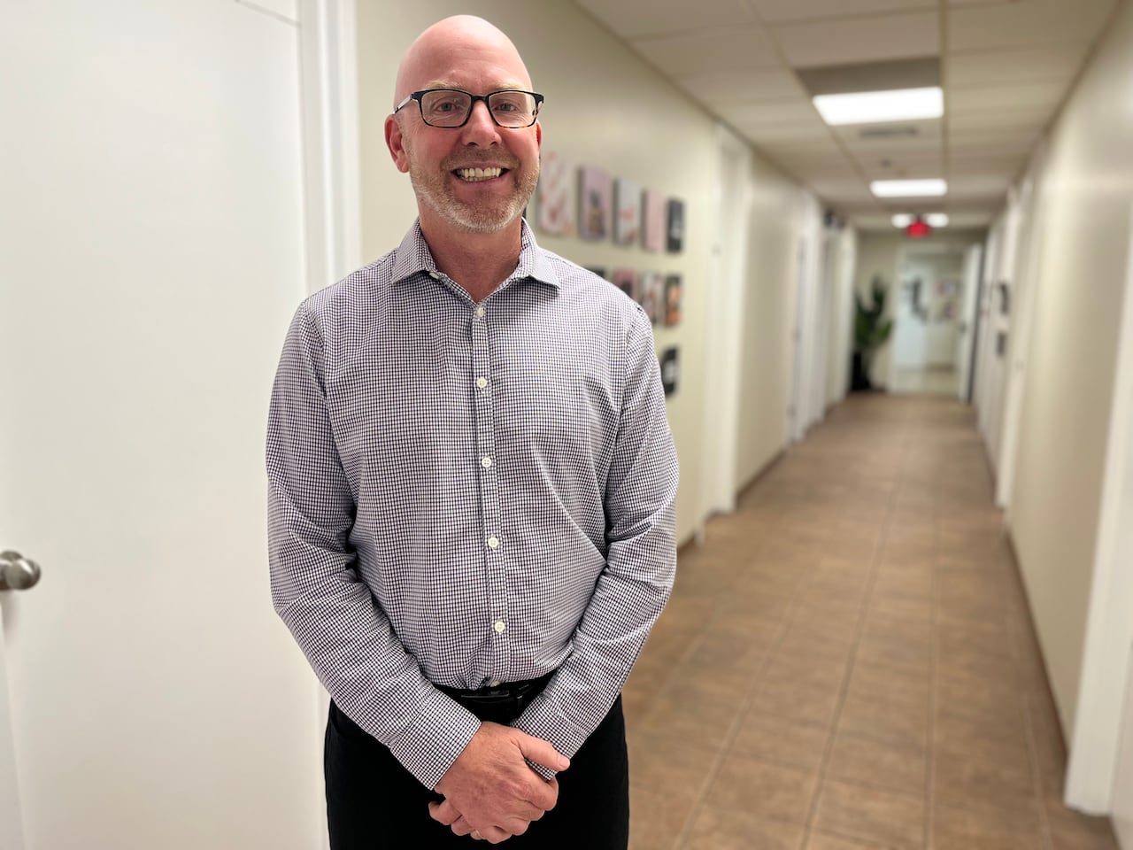 A man stands in an office hall way smiling at the camera.