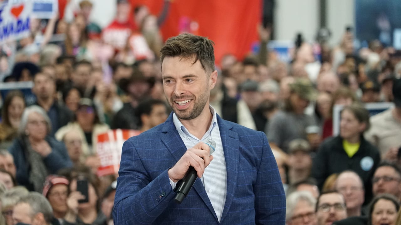 Man with microphone stands successful  beforehand   of a ample  assemblage  with a Canada emblem  successful  the background
