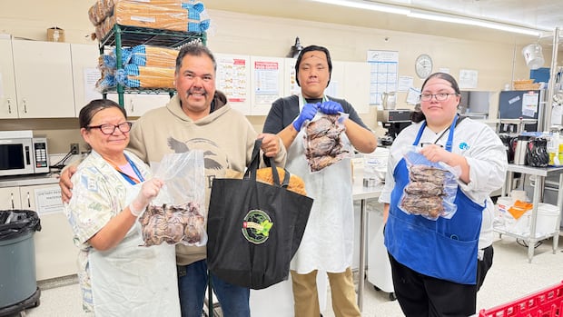 A group of four stand smiling towards the camera. Three of them are wearing hair nets and aprons holding up ducks that have been vacuumed sealed