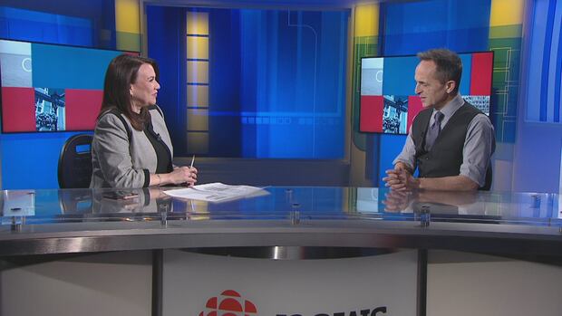 Louise Martin sits across from Brent Macdonald on the set of CBC News: Compass. A man and a woman sit across from each other on a TV news set.
