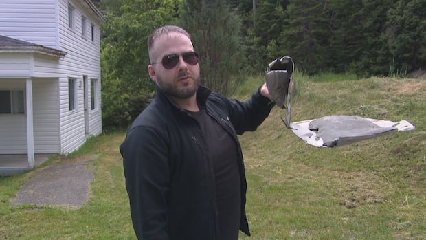 A man wearing sunglasses holds up a broken piece from his car