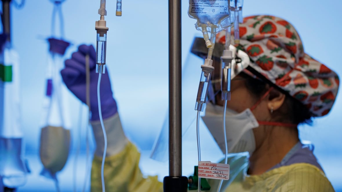 A nurse, wearing a yellow coat and a red and white cap, adjusts the IV cords.