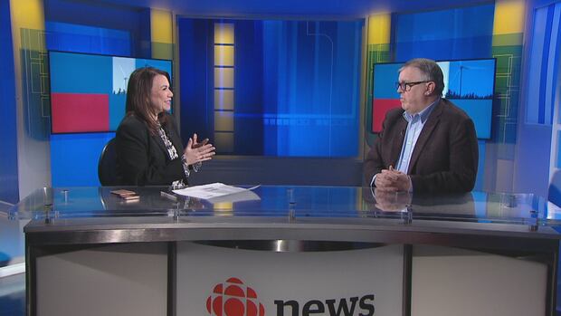 Louise Martin sits across from Steven Myers on the set of CBC News: Compass. Woman and man talk on a TV news set.