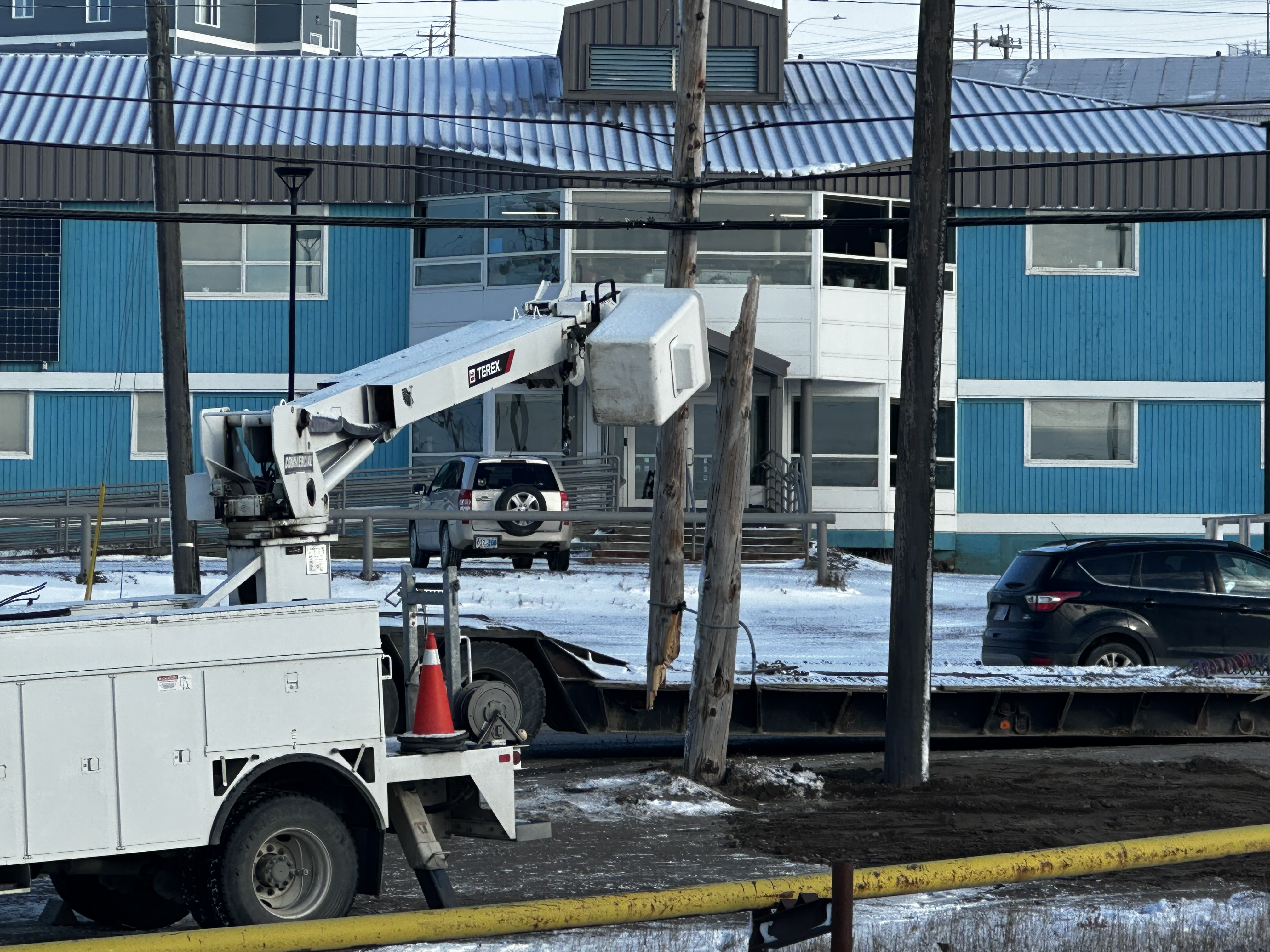 A broken power pole in downtown Iqaluit created a power outage on Oct. 11, 2025. A machine near a broken power pole in front of a blue building