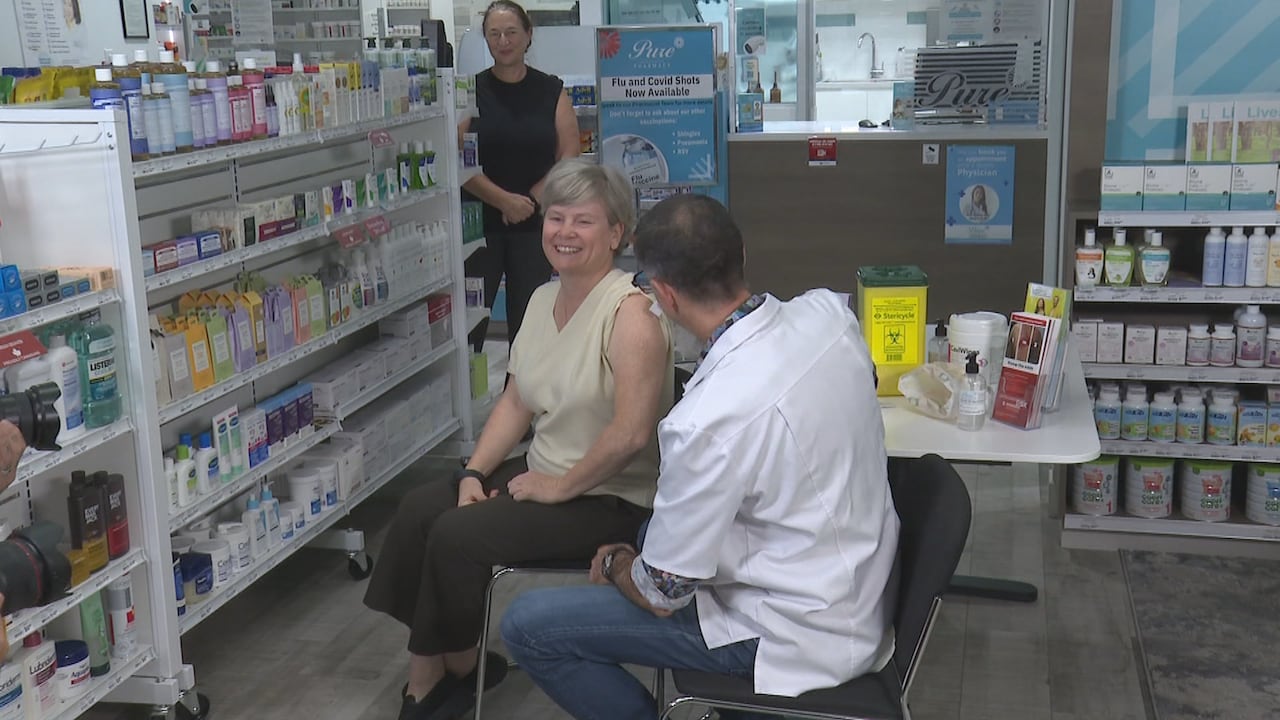 A woman prepares to be vaccinated by a man wearing a white coat