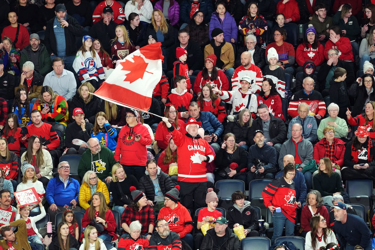 A fan waves a Canadian flag inside a hockey arena.