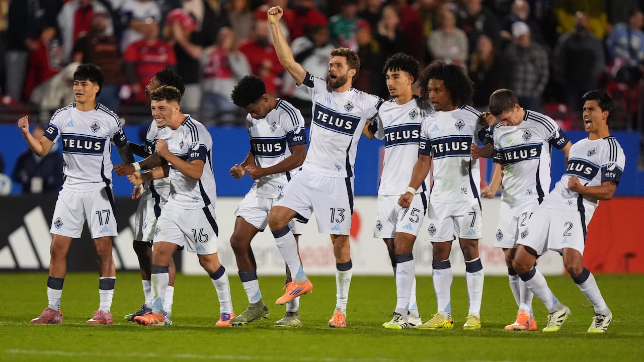 A group of soccer players who are lined up celebrate and pump their fists.