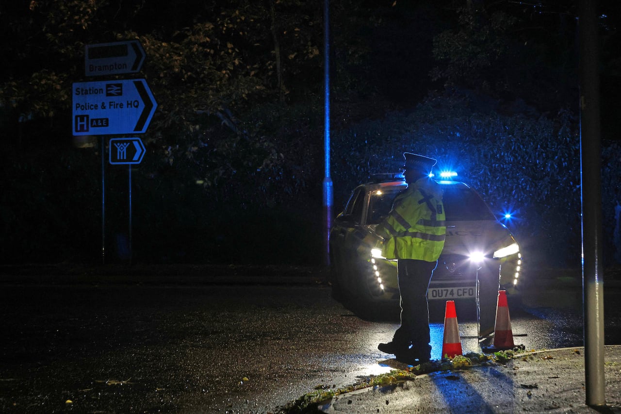 A police officer stands guard next to a vehicle with flashing ilghts.