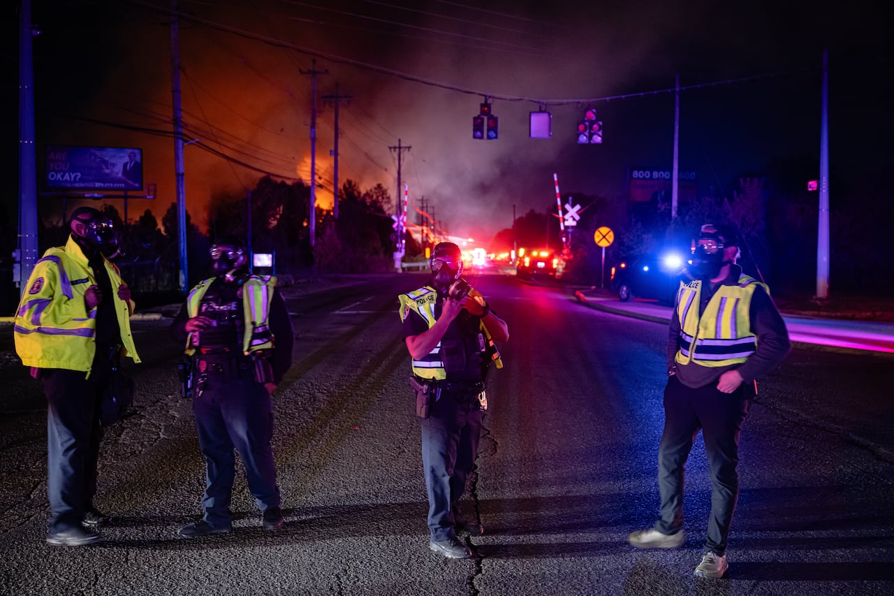 Law enforcement officers seen with flames in the distance.