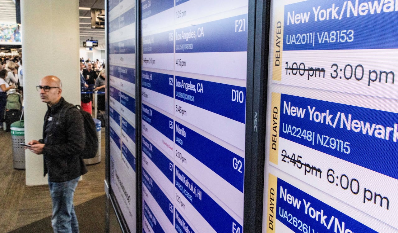 A passenger stands by a screen showing delayed flights at an airport. 