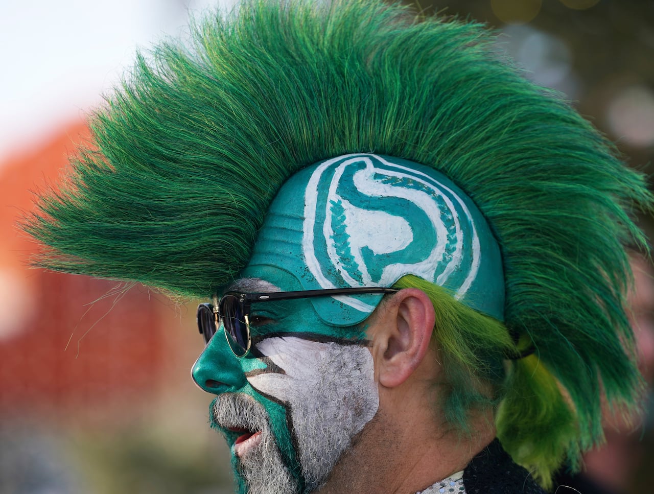 A man with green and white face paint and a green mohawk wig with the Saskatchewan Roughriders logo on the side.