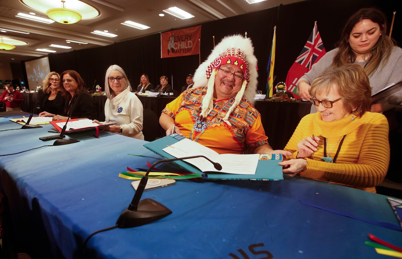 Several politicians and First Nations leaders sign a document at a news announcement.