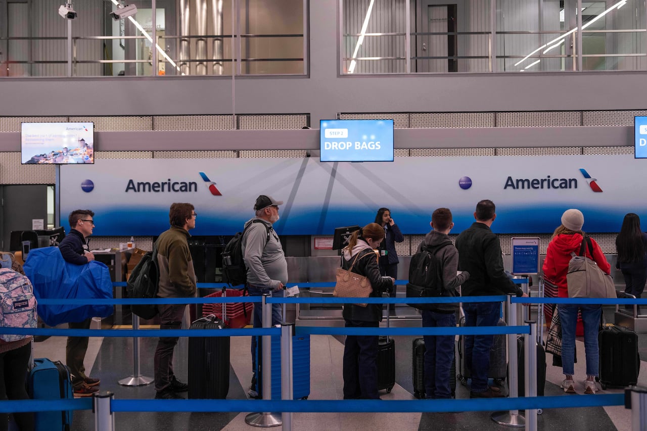 People wait in line with their luggage at the airport.