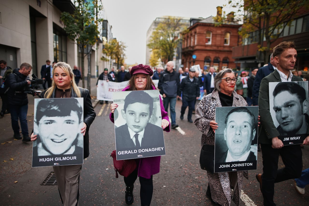 Several people, men and women, hold signs with pictures of other people in an outdoor demonstration on the street.