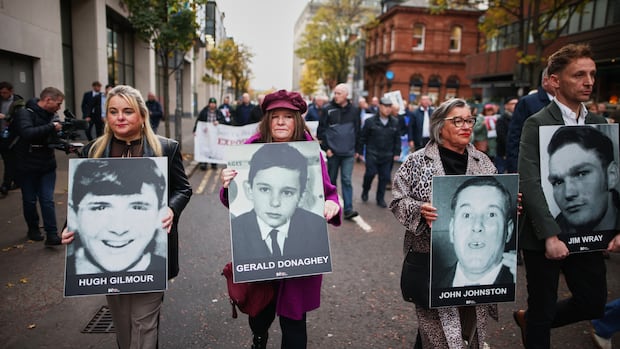 Relatives and supporters of the victims of the 1972 Bloody Sunday massacre march to Belfast Crown Court ahead of the verdict on the trial of a British soldier identified only as Soldier F, Belfast, in Northern Ireland, Thursday, Oct. 23, 2025. (AP Photo/Peter Morrison) Several people, men and women, hold up signs bearing images of other people in an outdoor demonstration on a street.