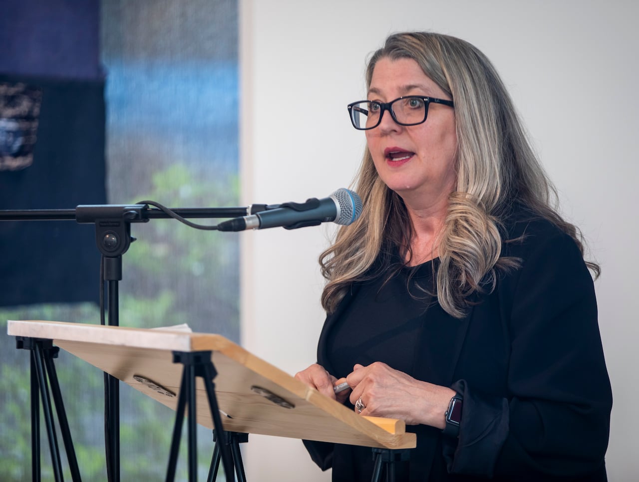 A white woman with blond hair speaks at a podium.