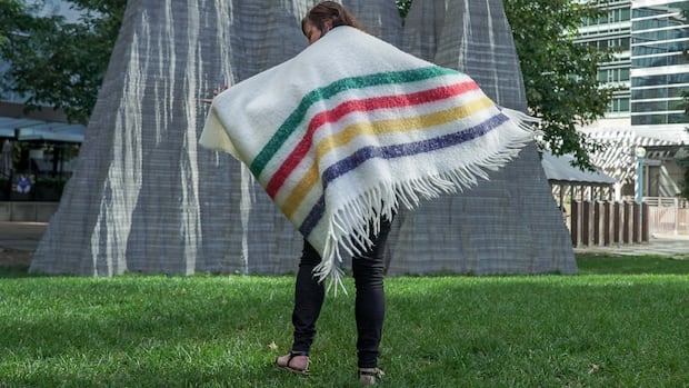 A woman wearing a colourful striped blanket is shown outside.