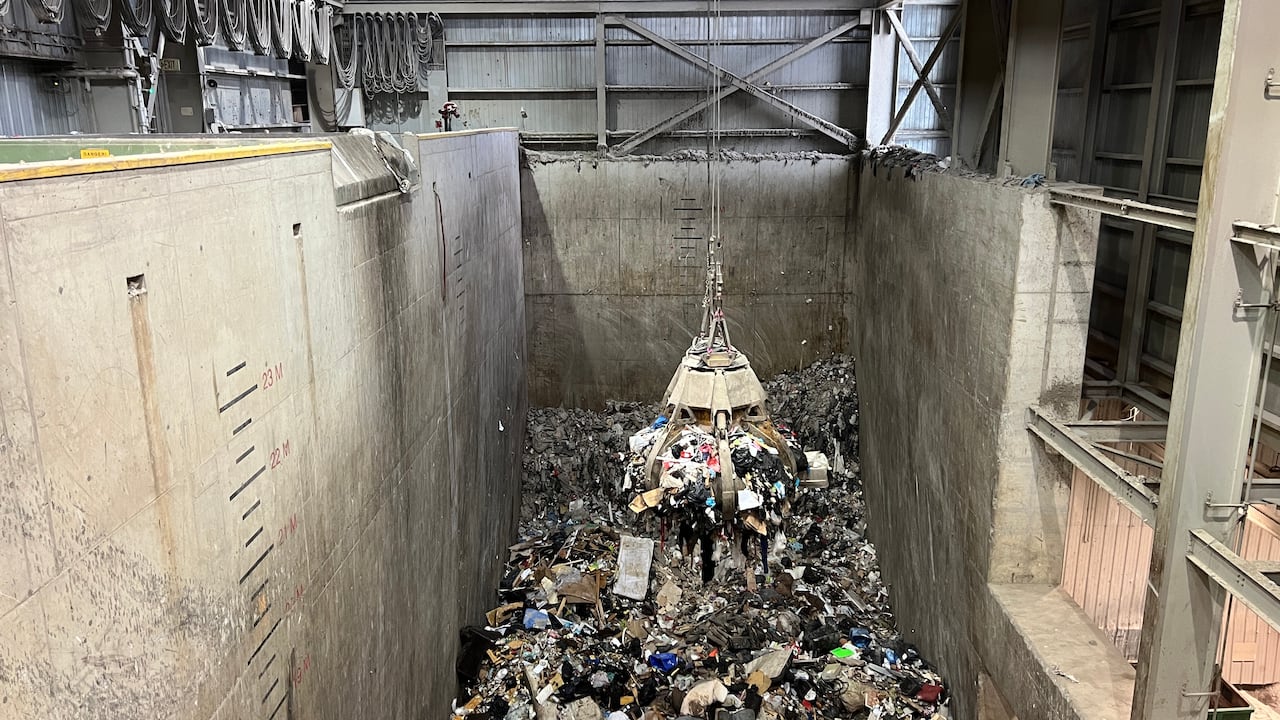 A large dangling grapple with metal arms is lifted into the air, while holding a black plastic bags and other garbage