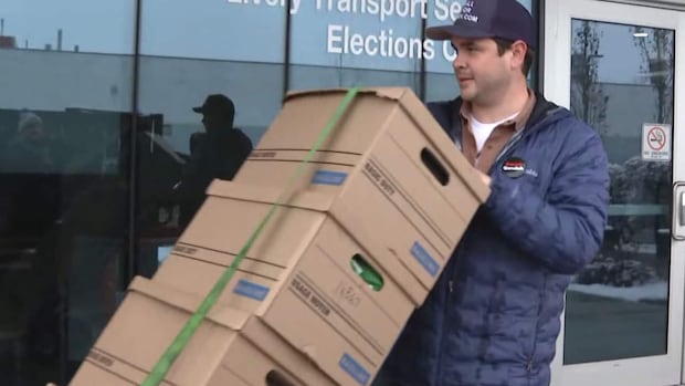 A man wheels a stack of cardboard boxes past a building.