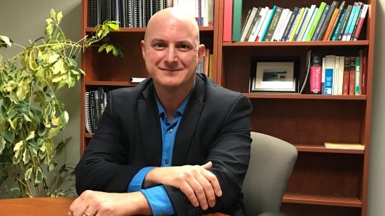 Bald man sitting at a desk, smiling at the camera. 