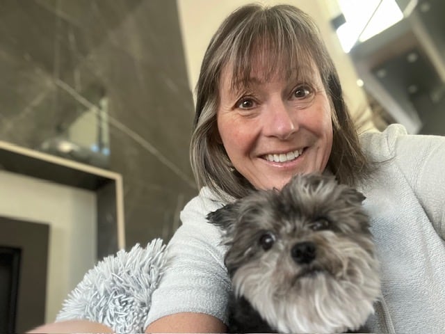 A smiling pistillate   with blond highlights successful  her hairsbreadth  poses for a selfie with a long-haired grey and achromatic  canine  nether  her chin. 
