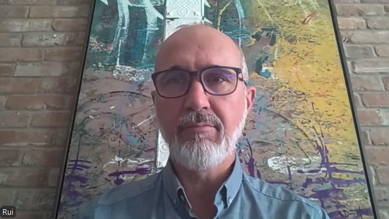 Rui sitting with an artistic painting and a brick wall behind him.