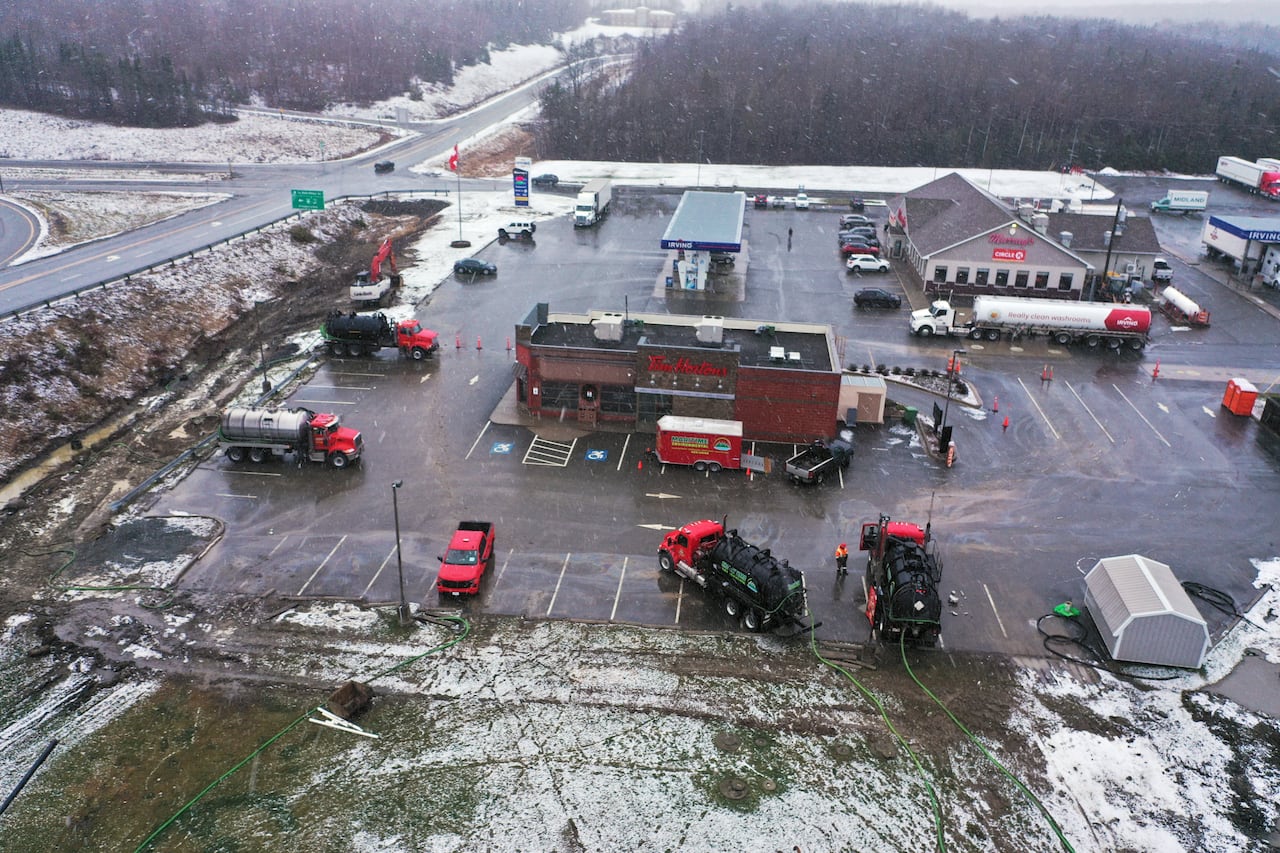 An aerial view of a Tim Hortons with four pump trucks surrounding it with green hoses running into the ditches nearby. Across the parking lot is in Irving oil gas station.