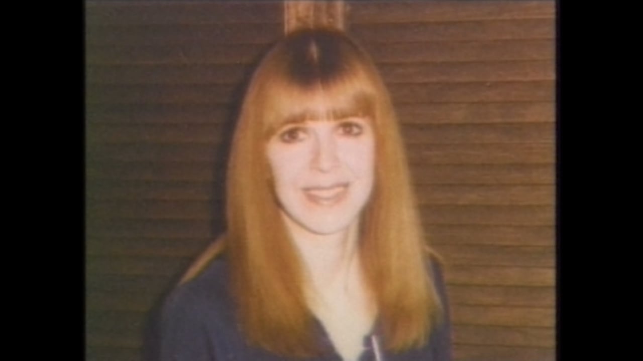 A woman with red hair, wearing a black sweater, smiles at the camera.