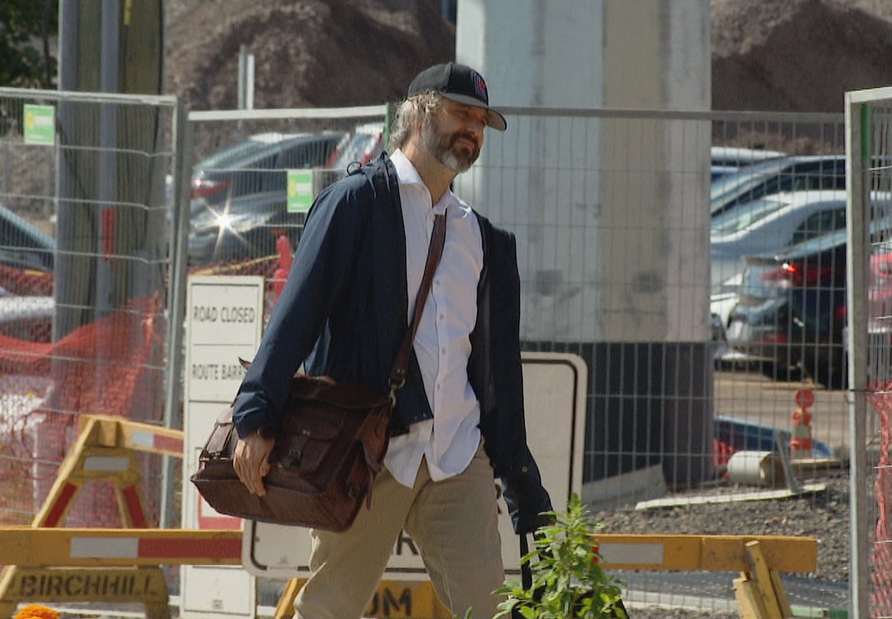 A man with a baseball cap walking on a sidewalk.
