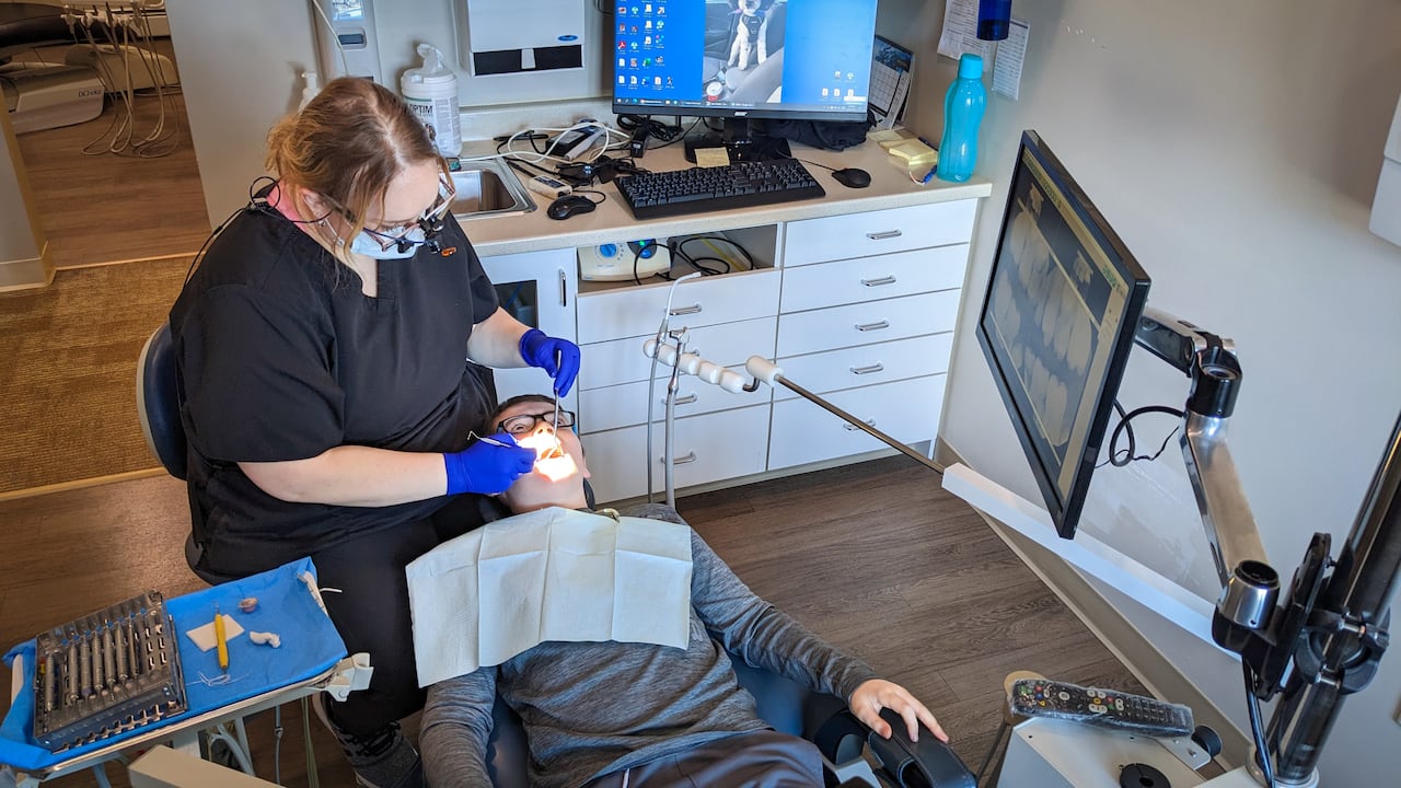 A dentist examine's a child's mouth while they sit in their chair.