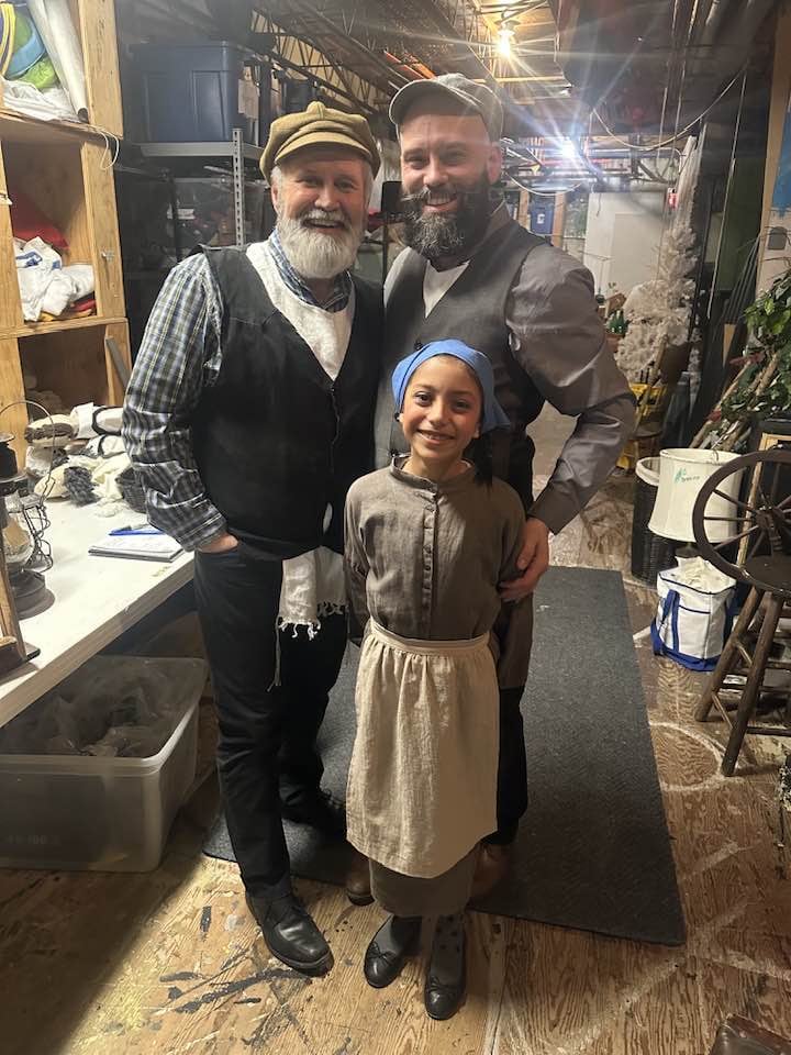 A man with a white beard, a man with a black beard, and a girl stand together