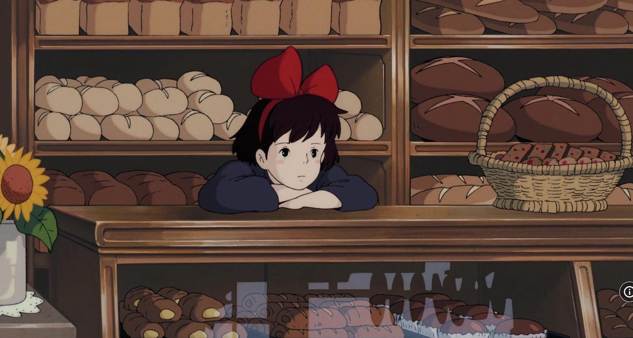 An illustration of a girl leaning on a pastry counter in a bakery with a wall of bread behind her. 