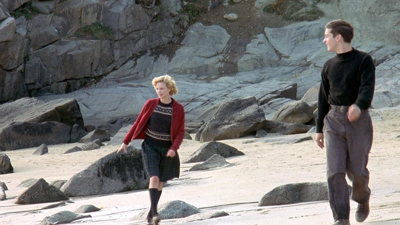 A man and a woman in fall clothing walking on the beach.