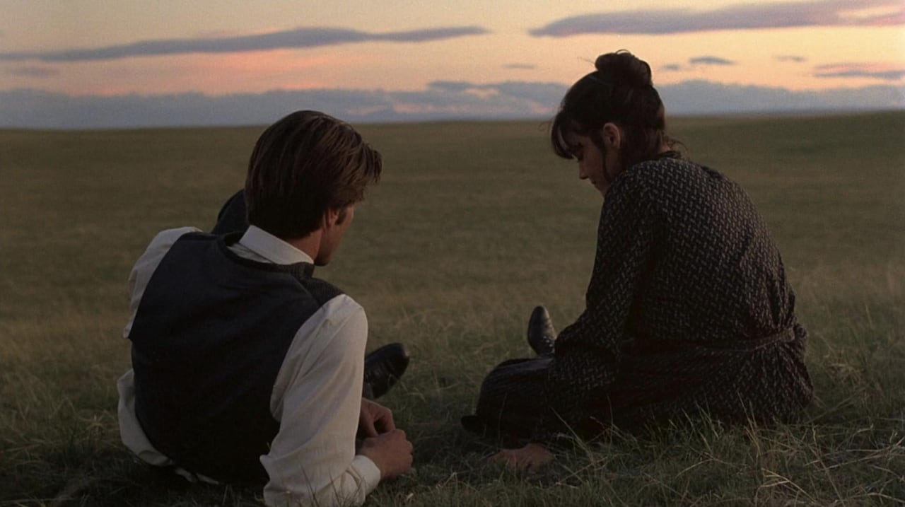 A man and a woman sitting in a field at sunset.