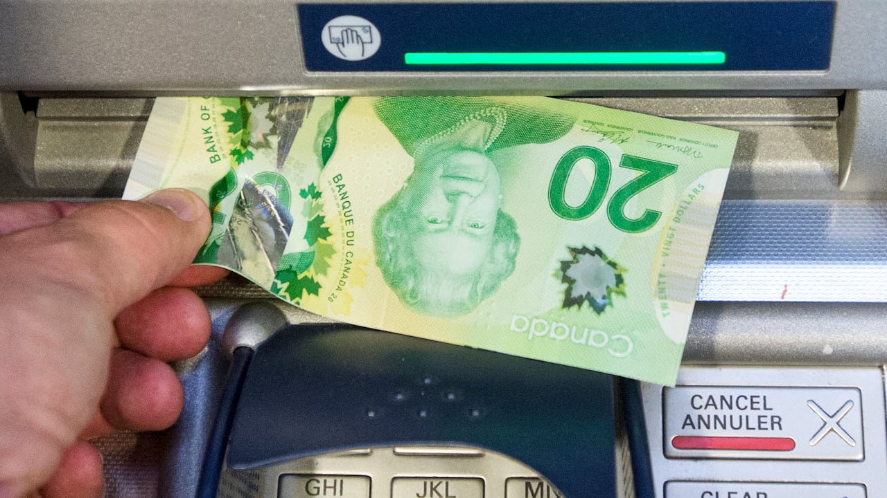 A manus is pulling a azygous 20 dollar measure from an ATM. The PIN pad is visible.