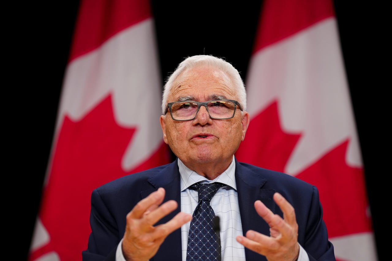 Un hombre sentado frente a una hilera de banderas canadienses.