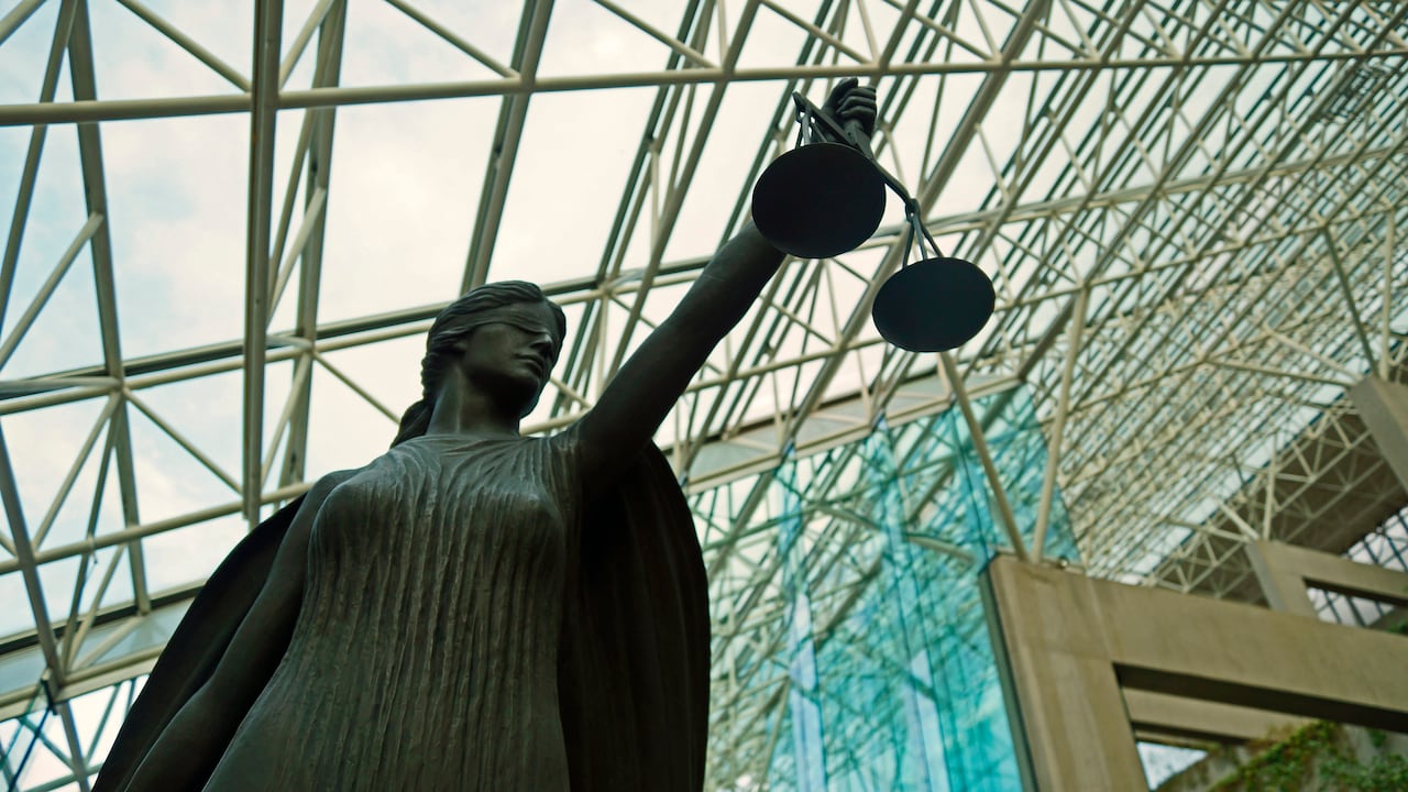 A statue of a blindfolded female figure holding a scale inside a glass-roofed building