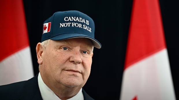 Ontario Premier Doug Ford, wearing a 'Canada Is Not For Sale' hat, speaks as he arrives for a first ministers meeting in Ottawa on Wednesday, Jan. 15, 2025. A man in a suit and ball cap stands for a photo.