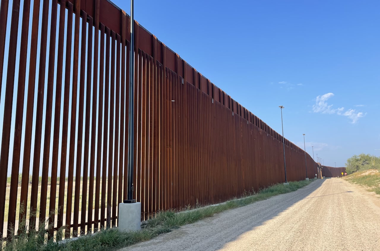 A tall iron fence goes into the distance, along a dusty road.